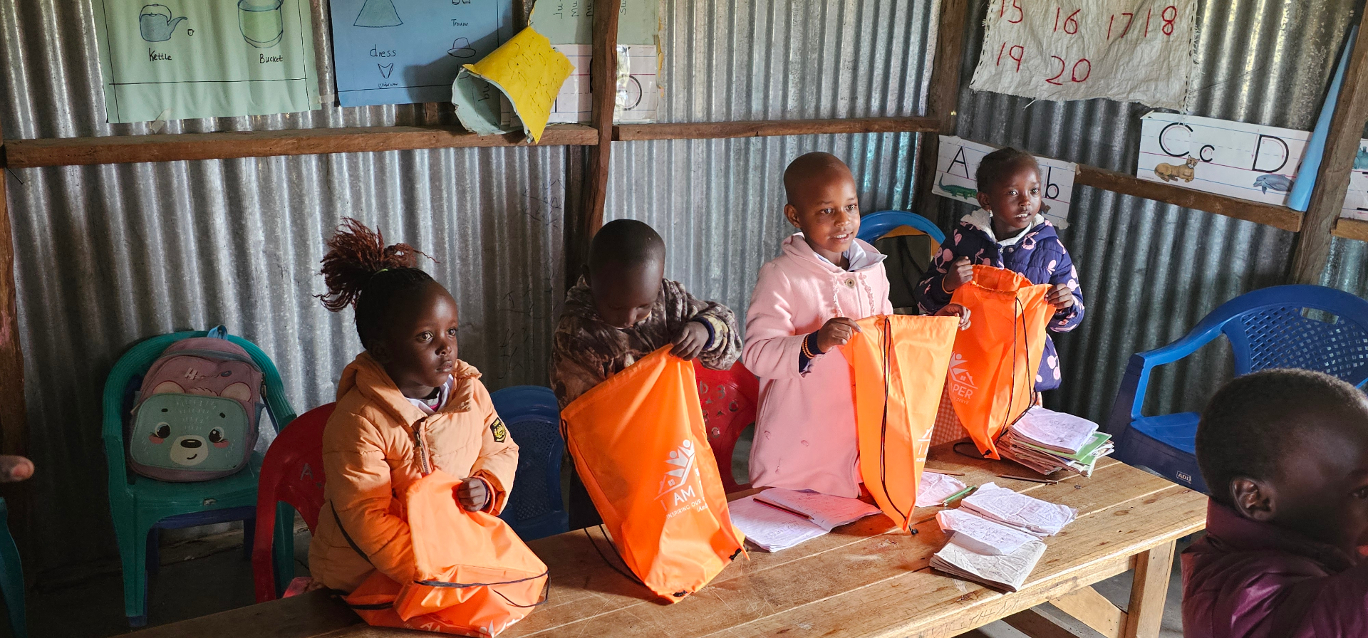 Young children receiving orange school backpacks at Empopongi school in Kenya
